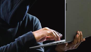 Hacker spy man one person black hoodie sitting hand holding credit card look computer laptop used login password attack security data digital internet network system night dark background copy space photo