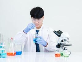 Portrait asian man student scientist wearing a doctor gown in the lab looking hand at chemist. caused by mixing reagents in scientific research laboratories with test tubes and microscope on the table photo