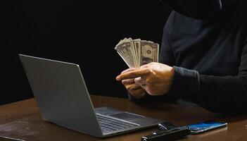 Hacker spy man one person black hoodie sitting hand holding credit card look computer laptop used login password attack security data digital internet network system night dark background copy space photo