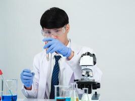 Portrait asian man student scientist wearing a doctor gown in the lab looking hand at chemist. caused by mixing reagents in scientific research laboratories with test tubes and microscope on the table photo