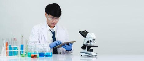 Portrait asian man student scientist wearing a doctor gown in the lab looking hand at chemist. caused by mixing reagents in scientific research laboratories with test tubes and microscope on the table photo