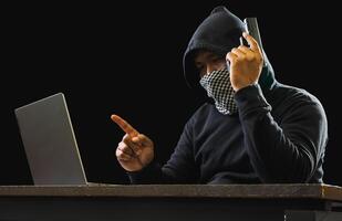 Hacker spy man one person black hoodie sitting hand holding credit card look computer laptop used login password attack security data digital internet network system night dark background copy space photo