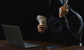 Hacker spy man one person black hoodie sitting hand holding credit card look computer laptop used login password attack security data digital internet network system night dark background copy space photo