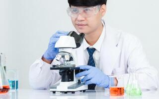 Portrait asian man student scientist wearing a doctor gown in the lab looking hand at chemist. caused by mixing reagents in scientific research laboratories with test tubes and microscope on the table photo