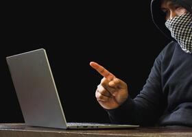 Hacker spy man one person black hoodie sitting hand holding credit card look computer laptop used login password attack security data digital internet network system night dark background copy space photo