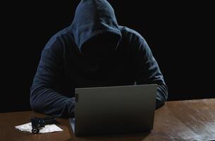 Hacker spy man one person black hoodie sitting hand holding credit card look computer laptop used login password attack security data digital internet network system night dark background copy space photo