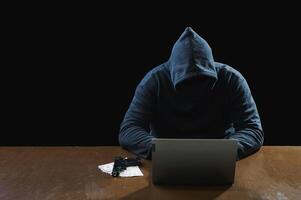 Hacker spy man one person black hoodie sitting hand holding credit card look computer laptop used login password attack security data digital internet network system night dark background copy space photo