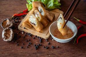Chinese vegetable spring rolls with chopstick to dip in sauce on wooden background photo