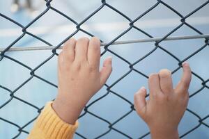 A childs hands gripping a chainlink fence tightly, symbolizing curiosity and exploration in youth photo