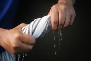 slow motion of Hands squeeze wet towel against black background. draining water from wet towel.. photo