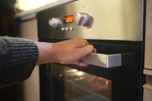 A person is using their hand to open a modern oven, engaging in culinary activities at home photo