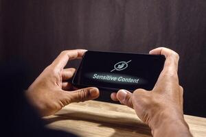 Man using a smartphone with eye crossed sign on screen. Explicit content in social media or website. Restricted content. photo