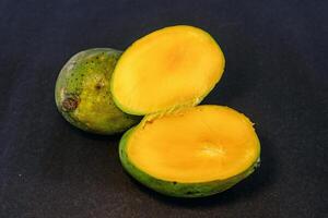 Ripe local Indonesian mango with cut in half isolated on dark background photo