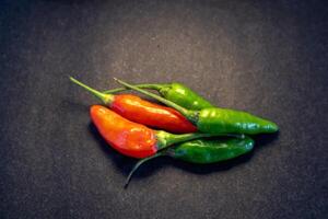 Pile of red and green cayenne pepper isolated on dark background photo