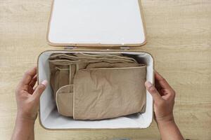 Someone is meticulously organizing garments in a storage container on a table made of wood photo