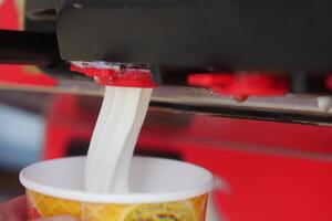 Closeup of Soft Serve Ice Cream Machine Dispensing Vanilla Ice Cream into a Cone photo