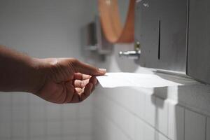 Hand Using Paper Towel Dispenser in a Hygienic Public Restroom with Clean White Tiles photo