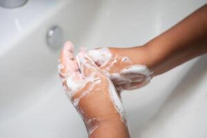 child making a cleansing gesture with soap and water on hands photo