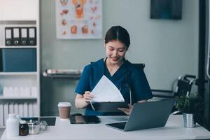 Female doctor writing in a notebook and holding a medicine bottle works at a computer while there were many medicine bottles on the table while sitting at a work desk photo