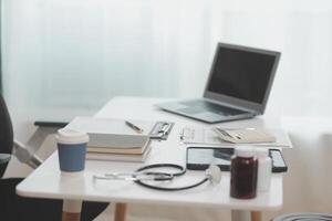 Doctor's working on laptop computer, writing prescription clipboard with record information paper folders on desk in hospital or clinic, Healthcare and medical concept. Focus on stethoscope photo