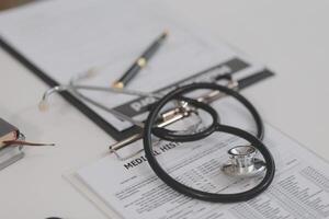 Doctor's working on laptop computer, writing prescription clipboard with record information paper folders on desk in hospital or clinic, Healthcare and medical concept. Focus on stethoscope photo