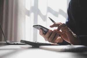 Side view shot of a man's hands using smart phone in interior, rear view of business man hands busy using cell phone at office desk, young male student typing on phone sitting at wooden table, flare photo