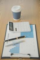 Close up view of simple workspace with laptop, notebooks, coffee cup and tree pot on white table with blurred office room background photo