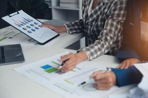 Group of confident business people point to graphs and charts to analyze market data, balance sheet, account, net profit to plan new sales strategies to increase production capacity. photo