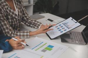Group of confident business people point to graphs and charts to analyze market data, balance sheet, account, net profit to plan new sales strategies to increase production capacity. photo