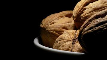 Walnuts nuts in a bowl at right of screen in rotation on black background video