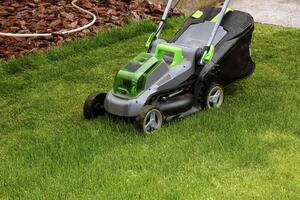 A young man is mowing a lawn with a lawn mower in his beautiful green floral summer garden photo