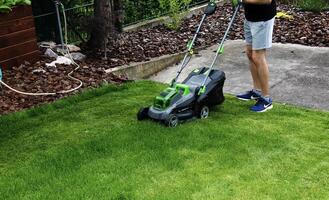 A young man is mowing a lawn with a lawn mower in his beautiful green floral summer garden photo