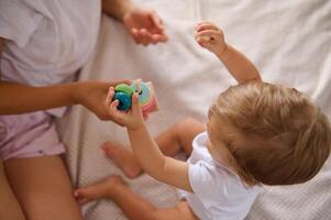 Baby playing with colorful stacking toy blocks with mother on cozy bed photo