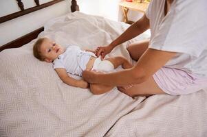Mother changing diaper of baby on bed in cozy home setting photo