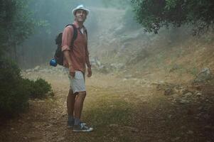 Man hiking in foggy forest path wearing hat and backpack photo