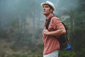 Man hiking in misty forest, wearing hat and backpack, enjoying outdoor adventure and nature exploration photo