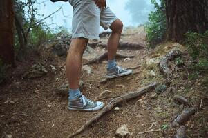 Man hiking on a forest trail wearing sneakers and shorts, surrounded by nature and trees photo