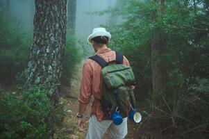 Backpacker walking through a misty forest trail with a backpack on a foggy day photo