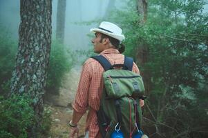 Man hiking in a foggy forest wearing a hat and backpack, exploring nature on a misty morning photo