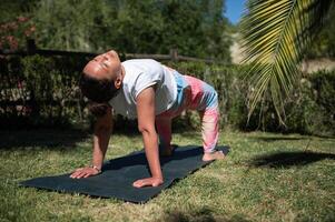 Woman practicing yoga outdoors on a sunny day in a serene garden setting photo