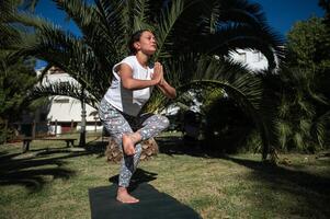 Woman practicing tree pose yoga outdoors in a serene park setting, surrounded by lush greenery photo