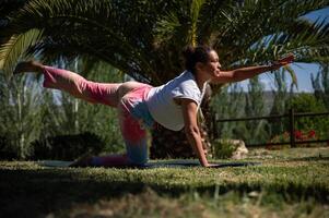 Young woman practicing yoga in a park performing bird dog pose on a sunny day photo