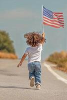 Child running and waving American flag on a rural road in daytime. photo