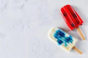 Red and blue popsicles on a white textured background, top view, summer concept, space for text. photo
