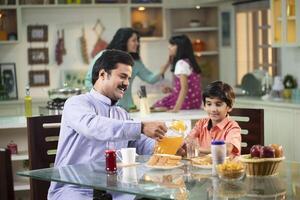 Mustache Dad Pouring Juice For Son At Table In Kitchen photo