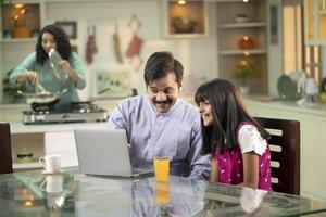 Father Daughter Surfing Internet With Laptop On Table At Kitchen photo