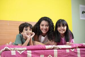 Happy Mom And Her Kids Lying On Bed While Posing In Front Of Camera photo