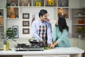 Caring Husband Cooking In Kitchen And Wife Smiling While Looking At Him photo