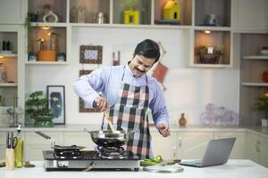 Loving Husband In Apron Learning To Cook While Watching Recipe On Laptop photo