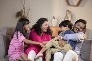 Father Mother And Kids Sitting On Sofa At Home Laughing While Spending Time Together photo